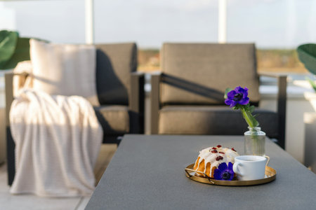 Close up of table with copy space near cup of morning coffee, sweet cake and single purple flower in...
