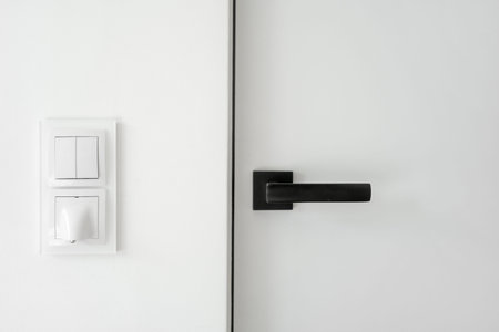 Close-up shot of a black door handle mounted on a white door, with a light switch on the copy space...