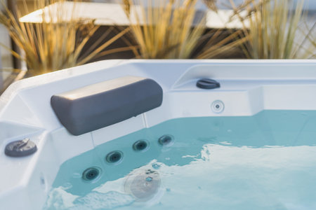 Modern bath with hydromassage jet, comfortable headrest and clear blue water. Hot tub on hotel...