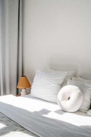A serene and minimal bedroom features a comfortable bed with white pillows, a soft round cushion,...