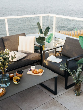 Vertical shot of modern patio with gray outdoor furniture and water view. Balcony with comfort...