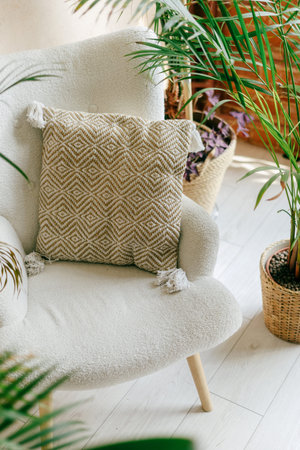 A soft armchair adorned with a patterned cushion sits next to vibrant indoor plants, creating a warm...