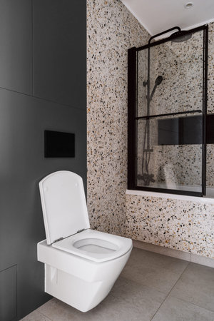 This contemporary bathroom showcases a sleek white toilet adjacent to a black-framed shower area,...