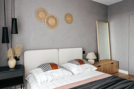 This cozy bedroom features a stylish bed with striped pillows, minimalist furniture, and decorative...