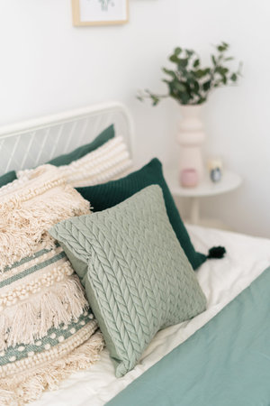 A serene bedroom setting features decorative pillows in various textures and colors, complemented by...