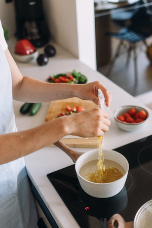 A woman focuses on preparing porridge, a healthy dish in her modern kitchen, pouring fresh...