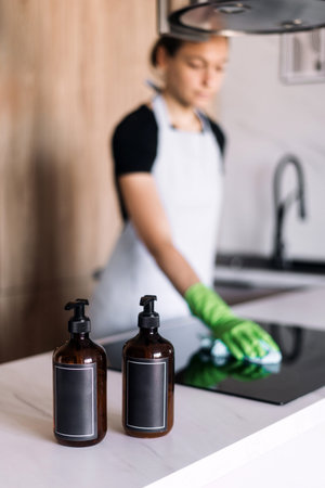 Labels on detergent bottles with copy space.A woman wearing apron and gloves cleaning an induction...