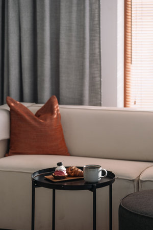 In a warm and inviting living room, a croissant, sweet pastry and a drink sit on a coffee table by a comfortable couch, creating a perfect spot for relaxation and enjoyment during a quiet afternoon.の写真素材