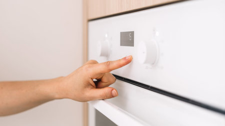 A person adjusts the settings on a white modern oven in a sleek kitchen. The interior features...