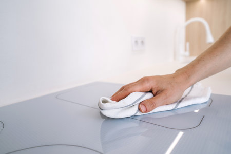 A hand gently wipes the glossy surface of an induction hob, keeping the modern kitchen clean. The sleek design reflects a contemporary lifestyle in a stylish apartment.の写真素材