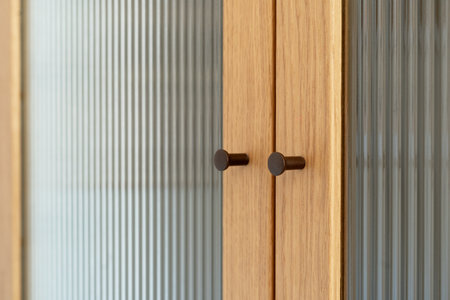 Interior detail showcases a light wood cabinet with reeded glass doors and bronze cylindrical knobs. The design of furniture in room is simple and contemporary.の写真素材