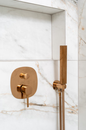 Close up shot of bathroom features a stylish gold faucet and shower system against a stunning white marble backdrop. The sleek design showcases contemporary elegance in residential living.の写真素材