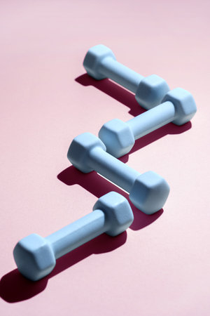 A set of light blue dumbbells is neatly arranged on a soft pastel pink background. Concepts of fitness activities and healthy lifestyles, perfect for any workout routine.の写真素材