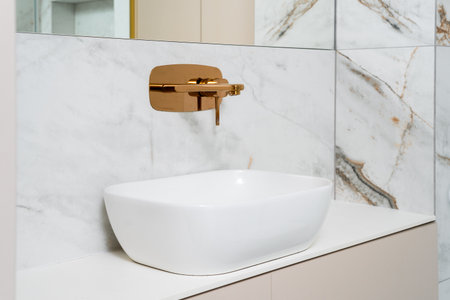 This contemporary bathroom features a sleek white ceramic sink against a marble backdrop. The golden faucet adds a touch of luxury to the home s morning self-care routine.の写真素材