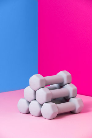 Colorful dumbbells are neatly stacked, showcasing versatile fitness equipment ideal for home workouts. The vibrant pink and blue backgrounds add a lively touch to any fitness routine.の写真素材