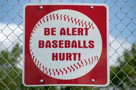 A sign posted on the backstop of a baseball field making people aware of flying baseballs.の写真素材