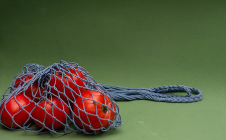 Tomatoes in blue shopping string bag on green backgroundの写真素材