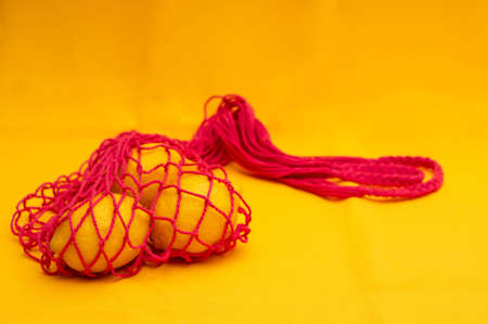 Lemons in red eco shopping string bag on yellow backgroundの写真素材
