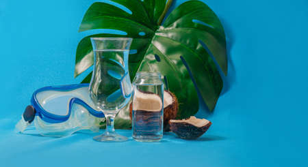 Diving mask, coconut halves and monstera leaf distorted through glasses with waterの写真素材