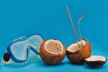 Diving mask and coconut halves with reusable drinking straws on blue backgroundの写真素材