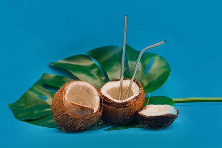 Coconut halves with reusable drinking straws on monstera leafの写真素材