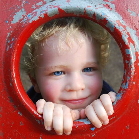 Cute boy peaking through playground equipment holeの写真素材
