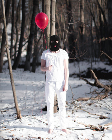 Young woman in black mask and white pants with red balloon in winter forestの写真素材