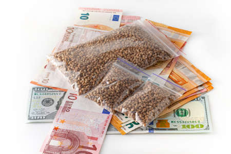Raw buckwheat groats in small transparent plastic bags, small dose, expensive, a lot of euro money. on white background. Crisis conceptの写真素材