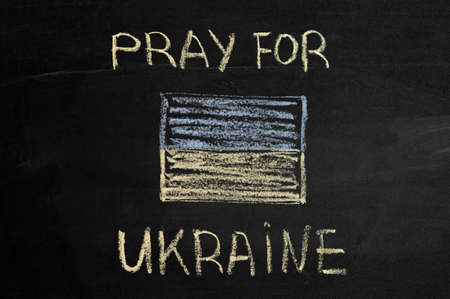 inscription Pray for Ukraine on a black board with chalk. ukraine flag drawn with chalk.の写真素材