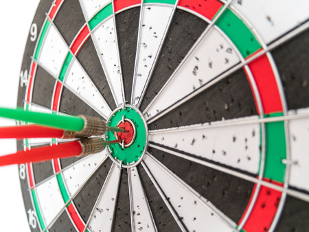 Close Up of Dart Holes on the Dart Board Due to Throwing Darts Multiple Times. Four Darts Hit the Red Bullseyeの写真素材