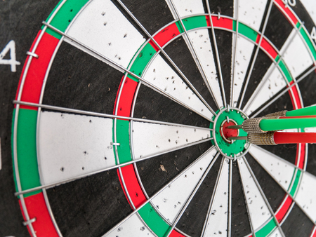 Close Up of Dart Holes on the Dart Board Due to Throwing Darts Multiple Times. Four Darts Hit the Red Bullseyeの写真素材