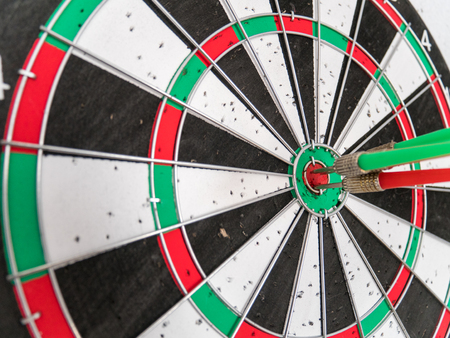 Close Up of Dart Holes on the Dart Board Due to Throwing Darts Multiple Times. Four Darts Hit the Red Bullseyeの写真素材