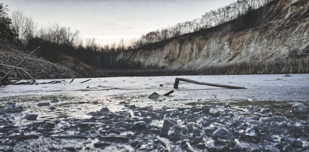 Quarry landscape. Plants in frost on frozen lake in stone quarry in winter. Frozen lake with ice and stone. Winter nature backdropの写真素材