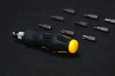 Black and yellow interchangable screwdriver with different bits surrounding. On dark dark background.の写真素材