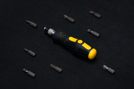 Black and yellow interchangable screwdriver with different bits surrounding. On dark dark background.の写真素材