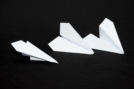 Three paper planes on dark background next to each other. Paper planes surrounding the scissors.の写真素材
