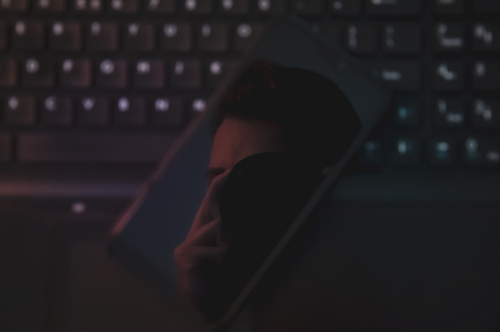 Man taking a photograph/selfie of himself in a reflective smartphone screen, lying on the laptop keyboardの写真素材