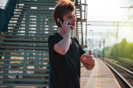 Young traveller man in black tshirt talking through the phone at the outdoor railway station during...