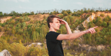 Young man in black tshirt pointing the direction with his finger while hiking in the mountains,...