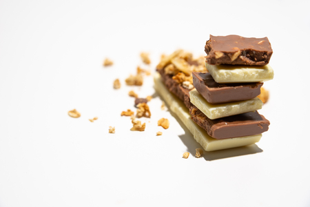 Side view on roughly cut chocolate bars stacked, with granola/ muesli in the background. Brown and white chocolate bars stacked, isolated on white background. Balanced diet concept.の写真素材