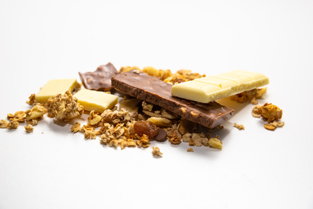 Side view on pile of granola/ muesli spilled among white. brown chocolate bars isolated on white background. Balanced and healthy diet concept.の写真素材