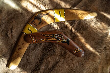 Two old boomerangs laying on the kangaroo skin, fur with wooden glossy table in the background. Souvenirs from Australia on display, shallow depth of field, warm colorsの写真素材