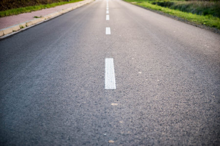 Empty road with white lines, with side walk on the left and grass on the both sides of the lane....