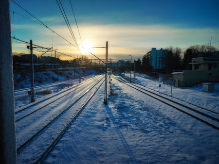 A serene winter morning with snow-covered railway tracks stretching into the distance. The sun rises perfectly, casting long shadows and creating a peaceful, tranquil atmosphere.の写真素材