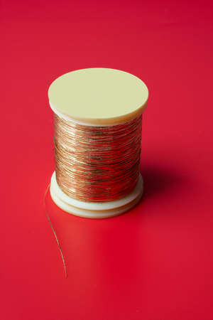 bobbin of golden thread on a red backgroundの写真素材