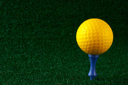 Yellow golfball and blue tee on grass backgroundの写真素材