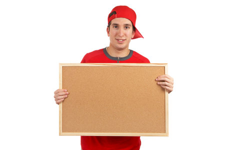 Curious teen with a red cap behind the empty corkboard on white backgroundの写真素材