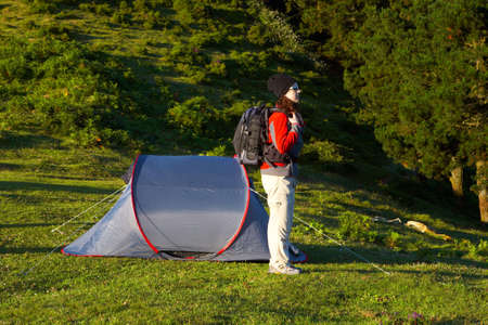 A girl with the black backpack next to her tent in the meadowの写真素材