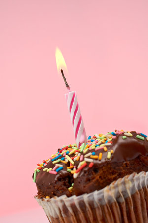 A tasty muffin chocolate with candle isolated on color background. Flame at focus and shallow DOFの写真素材