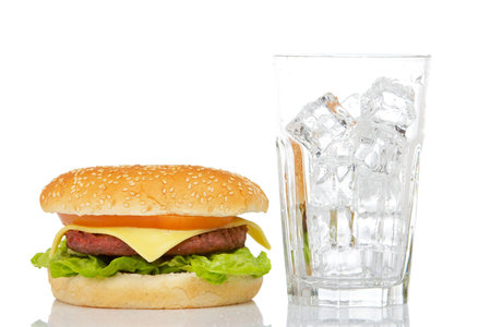 Cheeseburger and empty glass with ice cubes, reflected on white background. Shallow DOFの写真素材